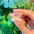 Cute pink starfish hair clip with polka dots and smiley face held against green leaves - Starfish
