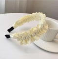 Détail d'un élégant serre-tête en satin plissé beige avec texture ondulée sur une table - Blanc Cassé