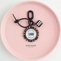 Detail of black poker chip keychain with dice and silicone strap on pink ceramic tray - Dice with Bead Ring / Black Brown-100 Value