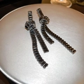Detail shot of long black zircon tassel earrings with geometric knot on a silver tray - Silver Needle - Black Knotted Tassel Style