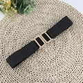 Detail of a black elastic woven belt featuring a textured gold metal buckle on a straw mat - Black