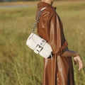 Sac baguette blanc minimaliste avec chaîne argentée porté à l'épaule en extérieur - Blanc