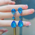 Macro detail of triple blue teardrop moissanite earrings held between fingertips - Sea Blue Zirconia