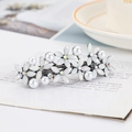 Silver flower hair clip with white pearls and rhinestones shown on an open book - White