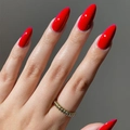 Glossy bright red almond-shaped long press-on nails shown on a real hand on grey background - Stiletto Shape / Glossy Bright Red