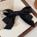 Close-up of black satin bow hair clip on a wooden tray with decorative textured paper - Hair Bow / Black