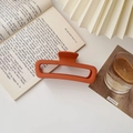 Close-up of matte terracotta rectangular hair claw clip placed on an open English book - Matte Large Square Orange