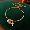 Dettaglio di un bracciale a croce dorato con perle e ciondoli a stella su velluto - Stile Croce e Perla Con Pendenti Multipli / Oro-Bianco