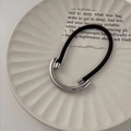 Detail eines minimalistischen schwarzen Haargummis mit poliertem silbernem Metallanhänger - Silber