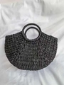 Close-up of a black half-moon straw handbag with a detailed woven pattern on white silk - Black
