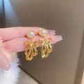 Close-up of golden bow-shaped pearl earrings held by hand showing delicate metal texture - Golden Pearl Bowknot (HE11464)
