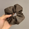Detail of brown satin scrunchie with soft ruffled texture and silky reflective fabric - Brown