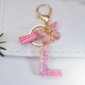 Detailed macro of resin letter L keychain with pink glitter butterfly and gold lobster clasp - Letter L