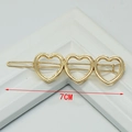 Detail showing 7cm golden metallic hair clip with three hollow heart shapes on white stand - Three Hearts Gold