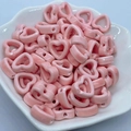 Close-up of pink heart-shaped ceramic beads in a white bowl for DIY jewelry making - Pink