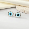 Macro view of blue evil eye stud earrings on white silk and decorative stones - Silver White Eye