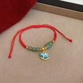 Dettaglio del bracciale rosso intrecciato con perle verdi e ciondolo cavallo a dondolo blu - Stile Cavallo Blu con Perla Verde Intrecciata in Corda Rossa (25#)
