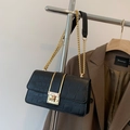 Detail of black crocodile pattern shoulder bag with gold chain strap on a chic blazer background - Black