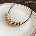 Detail view of twisted gold hoop necklace with black cord on a ceramic plate - Leather Cord Choker / Gold (Necklace)
