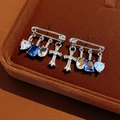 Close-up of silver safety pin earrings with blue zircon heart and cross charms - Safety Pin Cross Heart Style / Silver