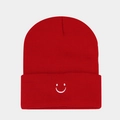 Close-up of a red knitted beanie featuring a white embroidered smiley face and ribbed texture - Red