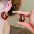 Detail of dark red triple-hoop C-shaped earrings showing glossy finish and ear fit - Red