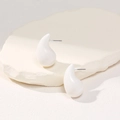 Detail view of white teardrop stud earrings on a textured stone aesthetic background - White