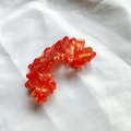 Eleganter hellorangefarbener Acetat-Haarclip mit Wellenmuster auf weißem Stoffhintergrund - Rot