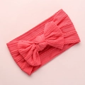 Detail of coral pink knitted baby headband featuring a large bow and soft cable texture - Watermelon red
