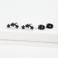 Detail view of black stainless steel triple star stud earrings on a white stone base - Three Star Style (164) / Black