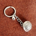 Detail of silver metal keychain with hollow sphere and small bell on brown fabric - Multi-size / Silver Bell