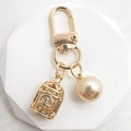 Golden birdcage and pearl keychain pendant on white minimalist display stand - Matte Gold Pearl + Birdcage