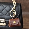 Mini brown leather coin purse keychain with gold hardware on a black quilted bag - Brown