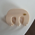 Detailed top view of beige French style claw clip with a golden Love logo on a white table - Wavy M-Shaped / Creamy White