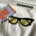 Detail view of cat eye sunglasses with black frame and yellow lenses on white fabric - Cat Eye / Black Frame Yellow Lens