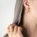 Orecchini a cerchio ritorti a C dorati e set di anelli a sigillo sulla modella - Oro