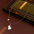 Detailopname van een gouden ketting met witte kalebas hanger en een kleine strik op stof - Witte Schelp / Goud