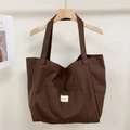 Detalle del bolso tote grande de lona marrón oscuro mostrando correas y bolsillo frontal - Ciruela Oscura
