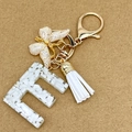 Letter E resin keychain with gold leaf butterfly and white tassel on paper background - Letter E