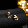 Detail view of irregular gold earrings featuring deep red oval gemstones on black stand - Gold Natural Garnet Stud Earrings