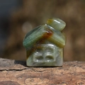 Macro shot of a small hand-carved natural green stone house on a rustic wood base - India Agate