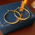 Detail van grote gouden oorringen op een luxe donkerblauwe geschenkdoos met warme verlichting - 18k Vergulde Gladde Ronde Oorbellen / Goud