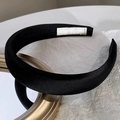 Detail of a thick black satin headband with smooth glossy finish and white inner label - Black