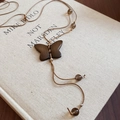 Macro di un ciondolo a farfalla in legno su una collana intrecciata con perle marroni - Ciondolo A Farfalla / Marrone