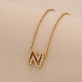 Detailed macro view of a gold initial M pendant necklace with sparkling cubic zirconia stones - Letter N