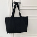 Detail of a black canvas tote bag hanging on a minimalist white door with black handle - Solid Black
