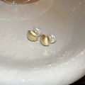 Close-up of gold matte geometric earrings with lustrous white pearls on a soft background - Circular Pearl Stud Earrings / Gold
