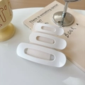 Detailed view of three white matte oval duckbill hair clips on cardstock background - White