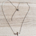 Detalle de un collar con colgante de cruz de acero inoxidable plateado sobre fondo madera - Plateado