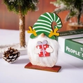 Détail d'un gnome de Noël en bois avec barbe en peluche blanche et boîte cadeau rouge - Chapeau vert à rayures/Tenant une boîte cadeau / Style Chapeau Vert